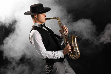 Male artist playing saxophone and smoke on black background