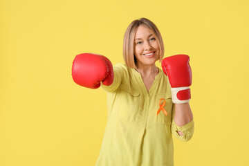 Happy mature woman in boxing gloves with ribbon on yellow background. Multiple Sclerosis Awareness...