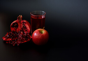 A glass of juice from a mixture of pomegranate and red apple on a black background, next to ripe fruits.