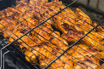 Delicious chicken frying on barbecue grill grate outdoor. Seasoning falling on fresh grilled chicken wings. Summer party food ideas. BBQ Juicy roasting chicken grill legs on grill grate 