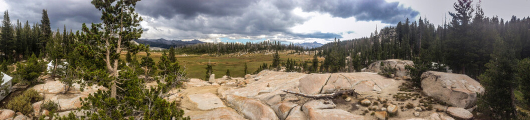 Panoramic sunny view of meadow and forest atop rocks on Yosemite National Park High Sierra Camp trail