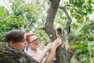 Two cheerful women playing with a kitten during a friends summer party in a country house