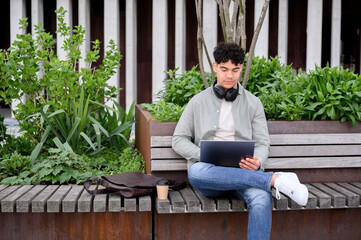 young man sitting on park bench using laptop
