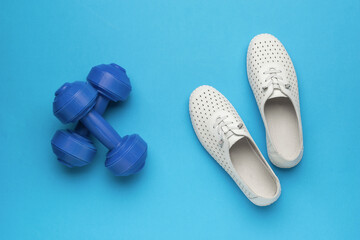 A pair of blue dumbbells and white athletic shoes on a blue background.