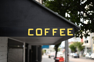 The word coffee written in yellow block letters, or capitals, on a black awning above a shop or cafe