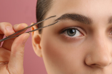 Eyebrow correction. Young woman with tweezers on pink background, closeup