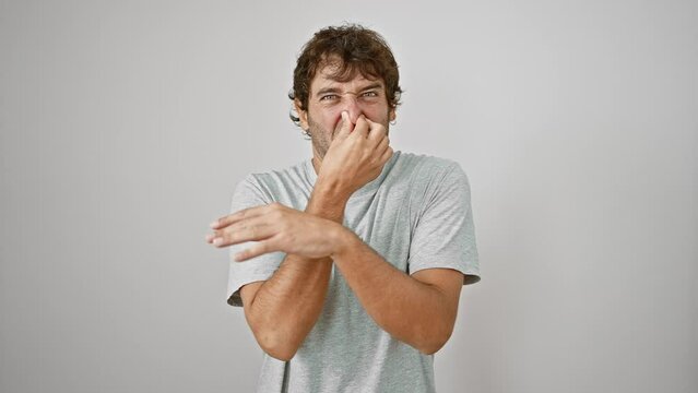 Shocked young man in t-shirt holding his nose in disgust - stinky, intolerable bad smell; an offensive stench over white isolated background