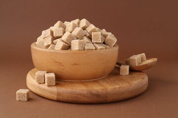Brown sugar cubes in bowl and spoon on color background