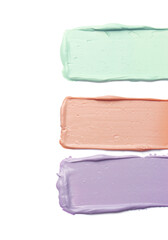 Strokes of pink, green and purple color correcting concealers on white background, top view