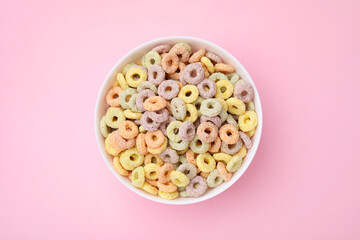 Tasty cereal rings in bowl on pink table, top view