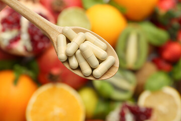 Vitamin pills in spoon over fresh fruits, top view