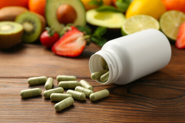 Vitamin pills, bottle and fresh fruits on wooden table