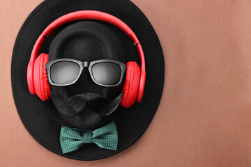 Man's face made of artificial mustache, sunglasses and hat on brown background, top view. Space for text