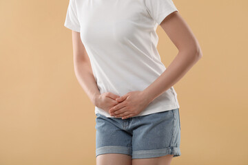 Woman suffering from cystitis on beige background, closeup