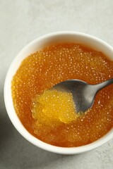 Fresh pike caviar in bowl and spoon on light grey table, top view