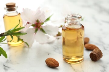 Almond oil in bottles, flower and nuts on white marble table, closeup