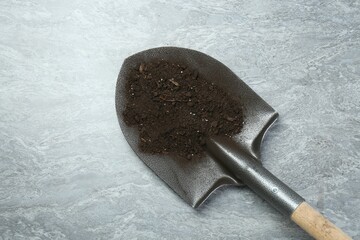 Metal shovel with fertile soil on gray textured surface, top view. Space for text