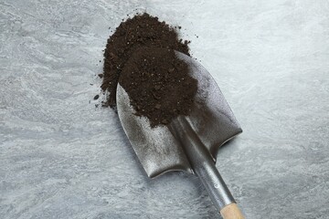 Metal shovel with fertile soil on gray textured surface, top view
