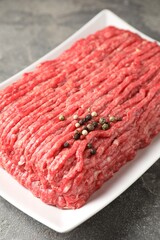 Raw ground meat and peppercorns on grey table, closeup