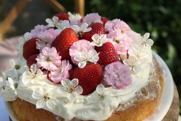 Delicious homemade cake decorated with fresh strawberries and spring flowers on table in garden, closeup