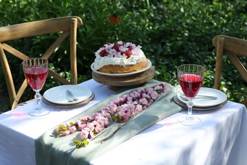 Beautiful spring flowers, delicious cake and wine glasses on table in garden
