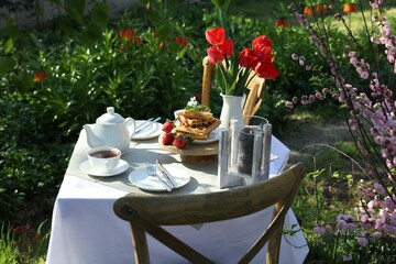 Beautiful bouquet of tulips and freshly baked waffles on table served for tea drinking in garden