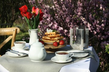 Beautiful bouquet of tulips and freshly baked waffles on table served for tea drinking in garden