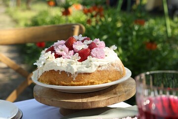 Delicious homemade cake decorated with fresh strawberries and spring flowers on table in garden