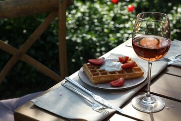 Delicious Belgian waffle with fresh strawberries and wine served on table in spring garden