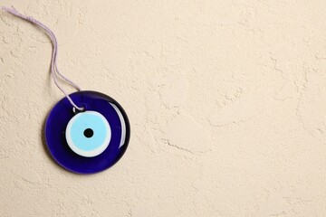 Evil eye amulet on beige textured table, top view. Space for text