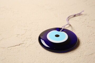Evil eye amulet on beige textured table, closeup. Space for text