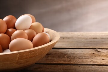Chicken eggs in bowl on wooden table, closeup. Space for text
