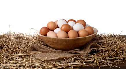 Fresh chicken eggs in bowl and dried straw on table against white background