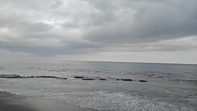 Playa con oleaje fuerte y horizonte con nubes grises y clima de lluvia