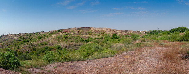 Panoramic view of wall of Mehrangarh fort from Rao Jodha desert rock park, Jodhpur, India. Green vegetation in the foreground with rocky landscape of the desert park.