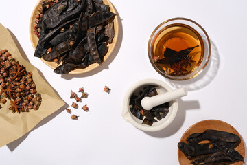 Photography with black locust and several herbs on white background, dish of herbs mixed, bowl of brown liquid, dried rose buds on vintage paper. Space for text and presentation, view from above
