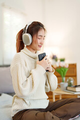 Young asian women in sweater wearing headphone to listening music and breathing while sitting on comfortable couch to relaxation and doing activity for spending time with slow life lifestyle at home