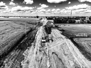High angle view of a road construction project starting in a corn field and leading into a city. 