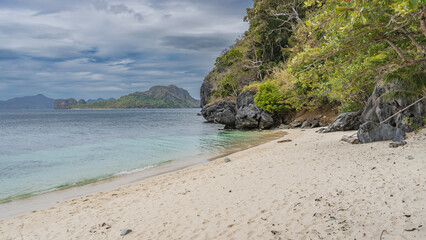 A secluded sandy beach on a tropical island. A calm turquoise ocean. Green vegetation on the...