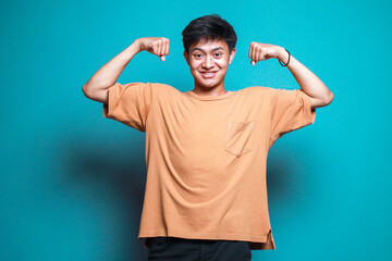 Portrait of young asian man showing hand muscle on blue background