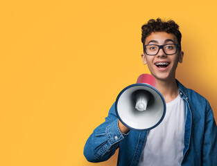 Funny happy brunette young man wear glasses dent dental tooth braces brackets advertise use mega phone megaphone loudspeaker open mouth, isolated over yellow background. Sales ad concept