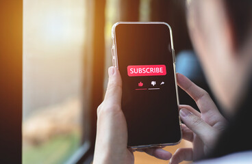 Close-up view of a woman using a smartphone to press red subscribe button on online media. Concepts...