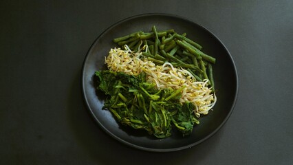 Urap, Indonesia traditional food served on plate with black background. Salad dish consist of...