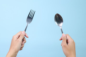 Woman hands holding spoon and fork isolated on blue background