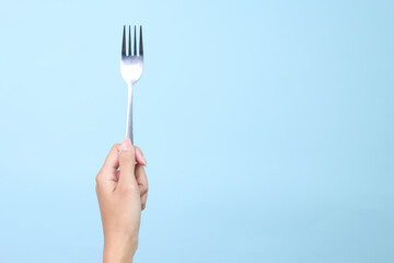 Woman's hand holds a metal fork on a blue background.