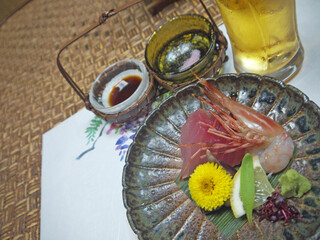 Gourmet shrimp and amberjack sashimi on ceramic plate decorated with yellow Chrysanthemum flower with beer glass in background