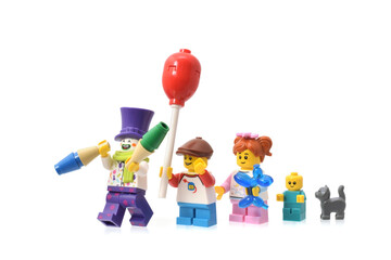 Fototapeta premium Lego minifigures clown in purple cup and girls, boy with balloon on the street parade or carnival. Editorial illustrative image of carnival.