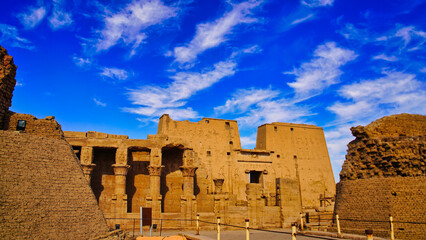 Beautiful cloud patterns and bright blue skies frame the floral columns and outer courtyard of the Temple of Horus at Edfu built during the Ptolemaic era between 237 to 57 BC near Aswan,Egypt - obrazy, fototapety, plakaty
