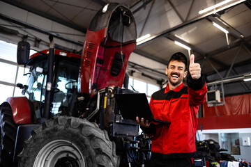 Tractor serviceman holding thumbs up inside workshop.