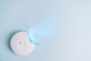 Home portable equipment with blue light for teeth whitening on blue background.